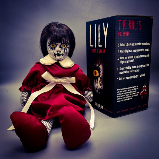 Horror-themed doll with red dress and black hair next to its packaging box on a dark background
